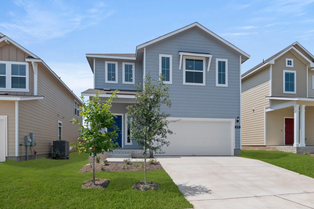 Exterior of a two-story blue home with a green landscape with trees.