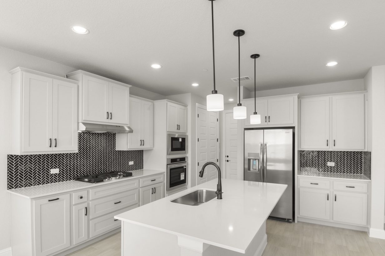 Kitchen interior with grey cabinets and white countertops with black backsplash tile and steel appliances.
