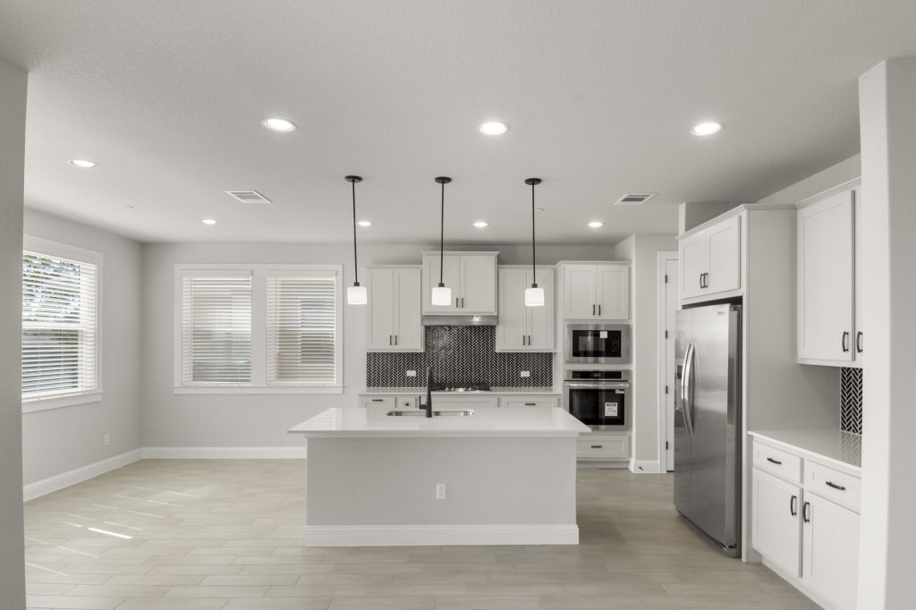 Kitchen interior with grey cabinets and white countertops with black backsplash tile and steel appliances.