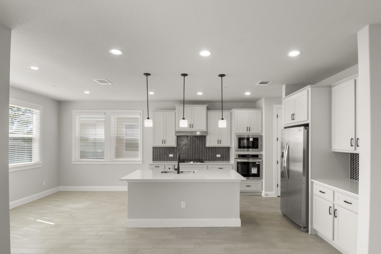 Kitchen interior with grey cabinets and white countertops with black backsplash tile and steel appliances.