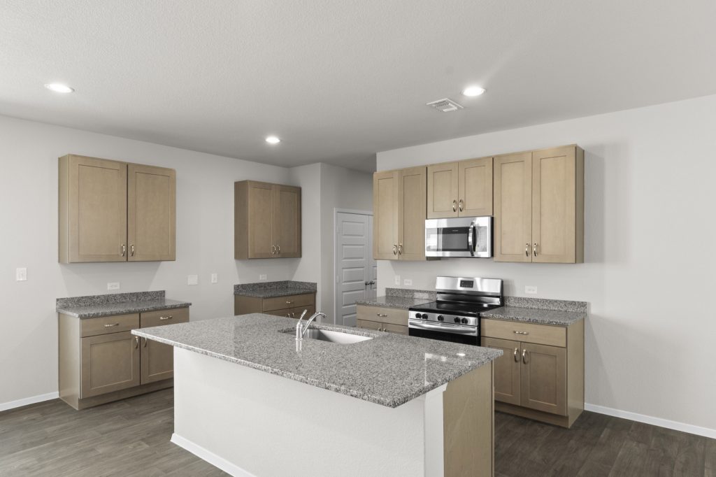 Interior image of kitchen with tan cabinets, an island, and granite countertops.