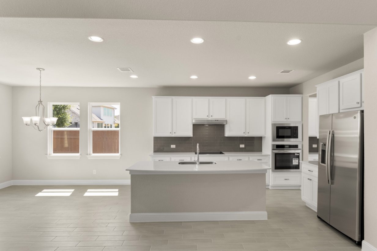 A Kitchen with white countertops, white cabinets, steel appliances, and gray blacksplash tile, white painted walls and vinyl flooring.