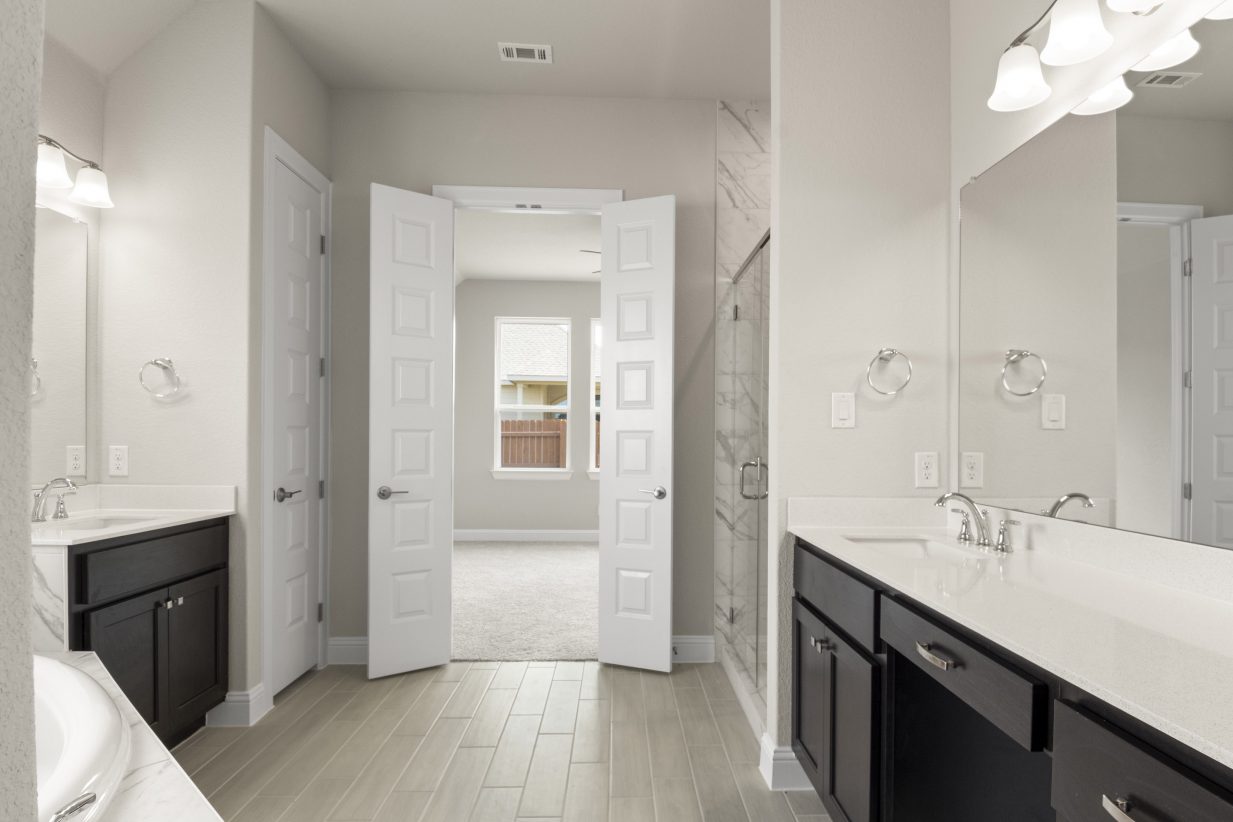 The primary bathroom with a glass shower with marble tiles, vanities with white countertops and dark brown cabinets, and vinyl flooring.
