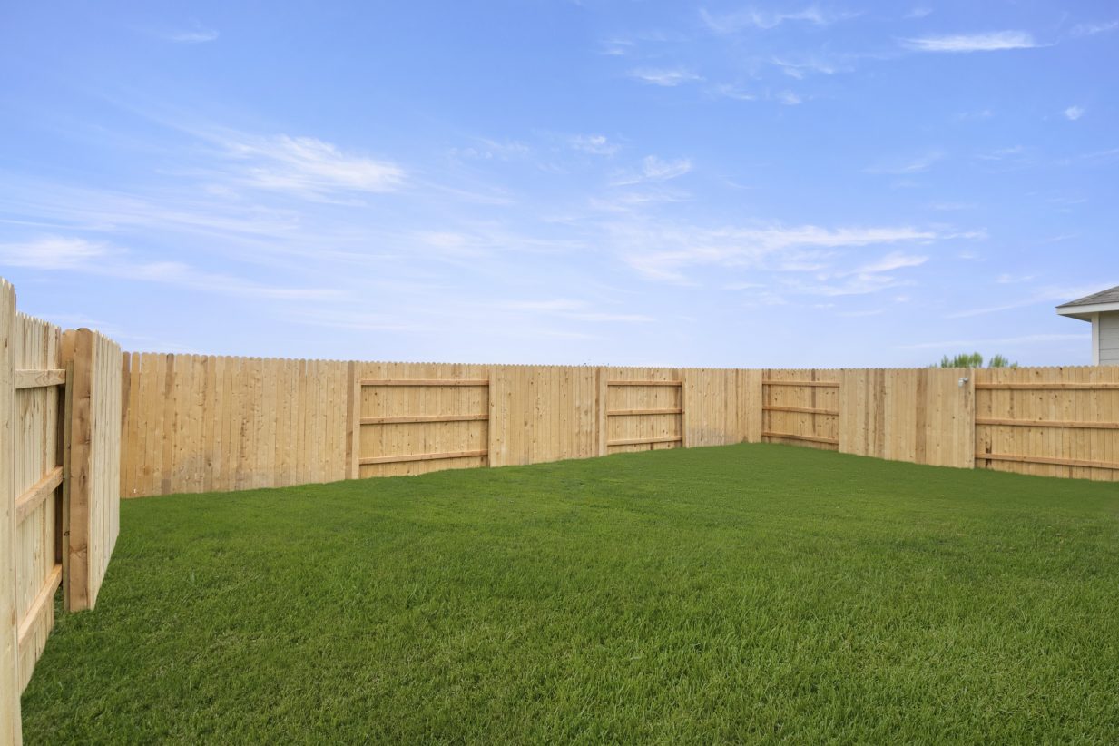Photo of home backyard with grass, wood fence, and sky