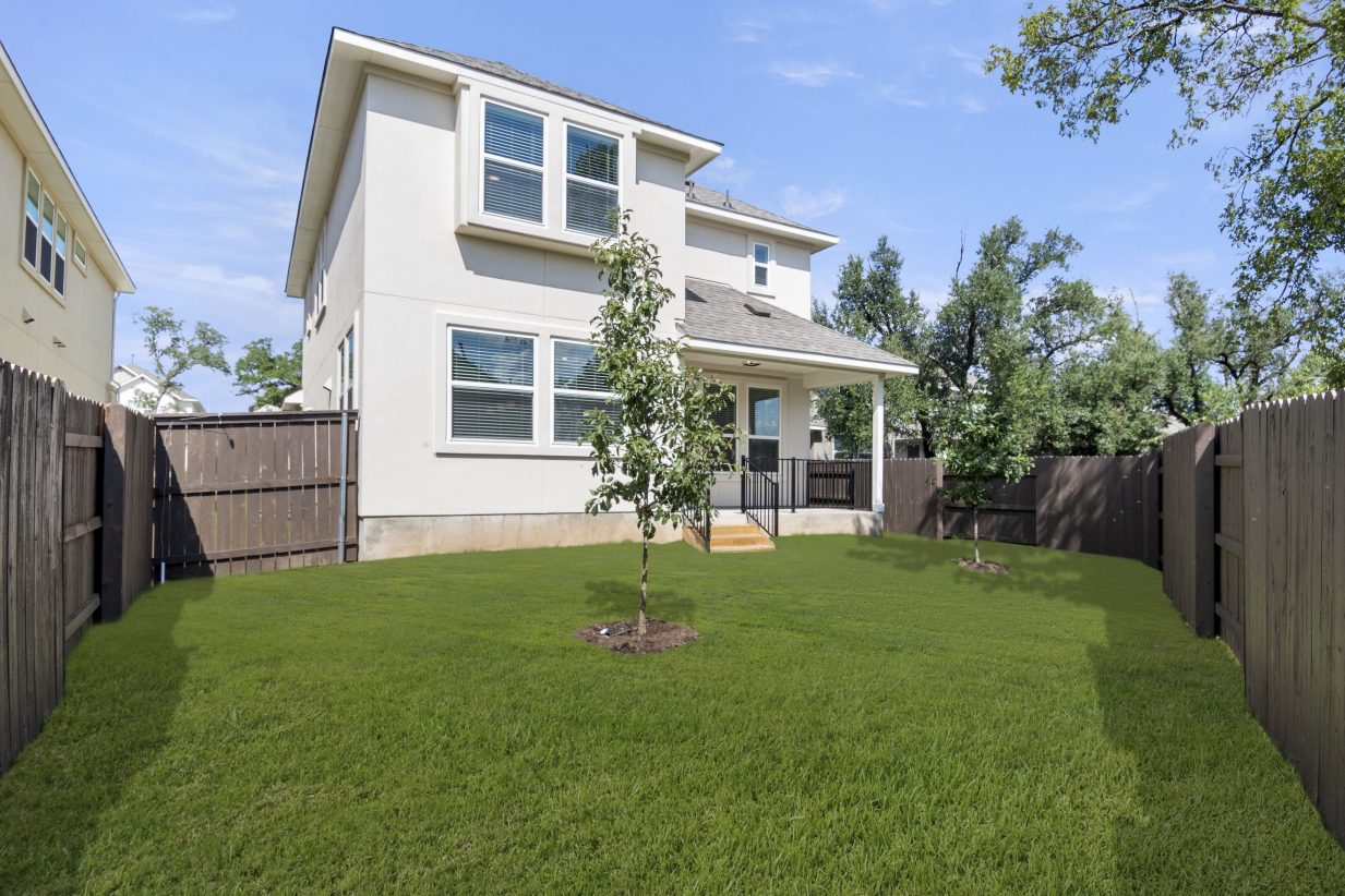 Exterior of the back of the two-story home with green landscape and brown fence.