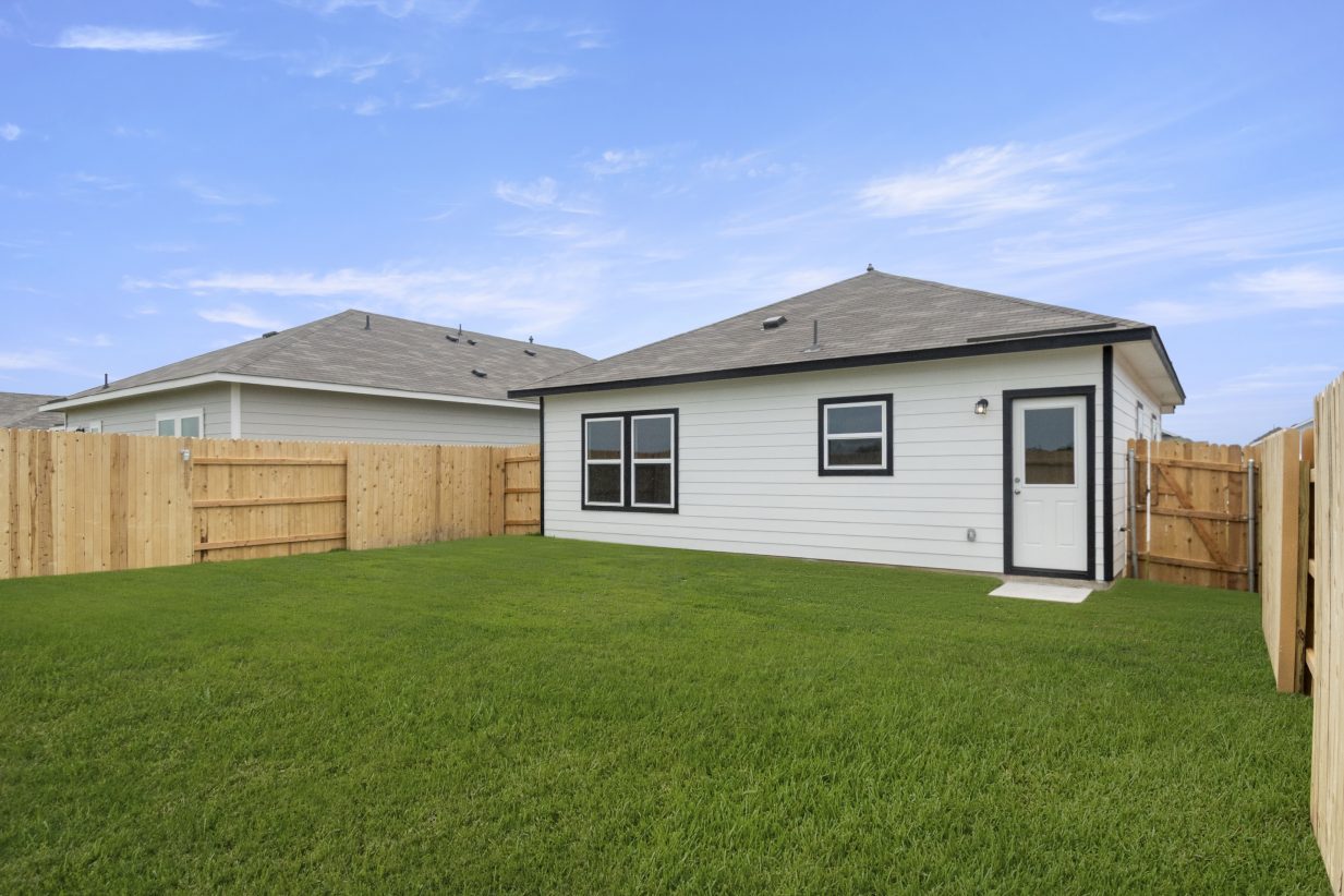 Photo of rear of black and white home with grass and fence