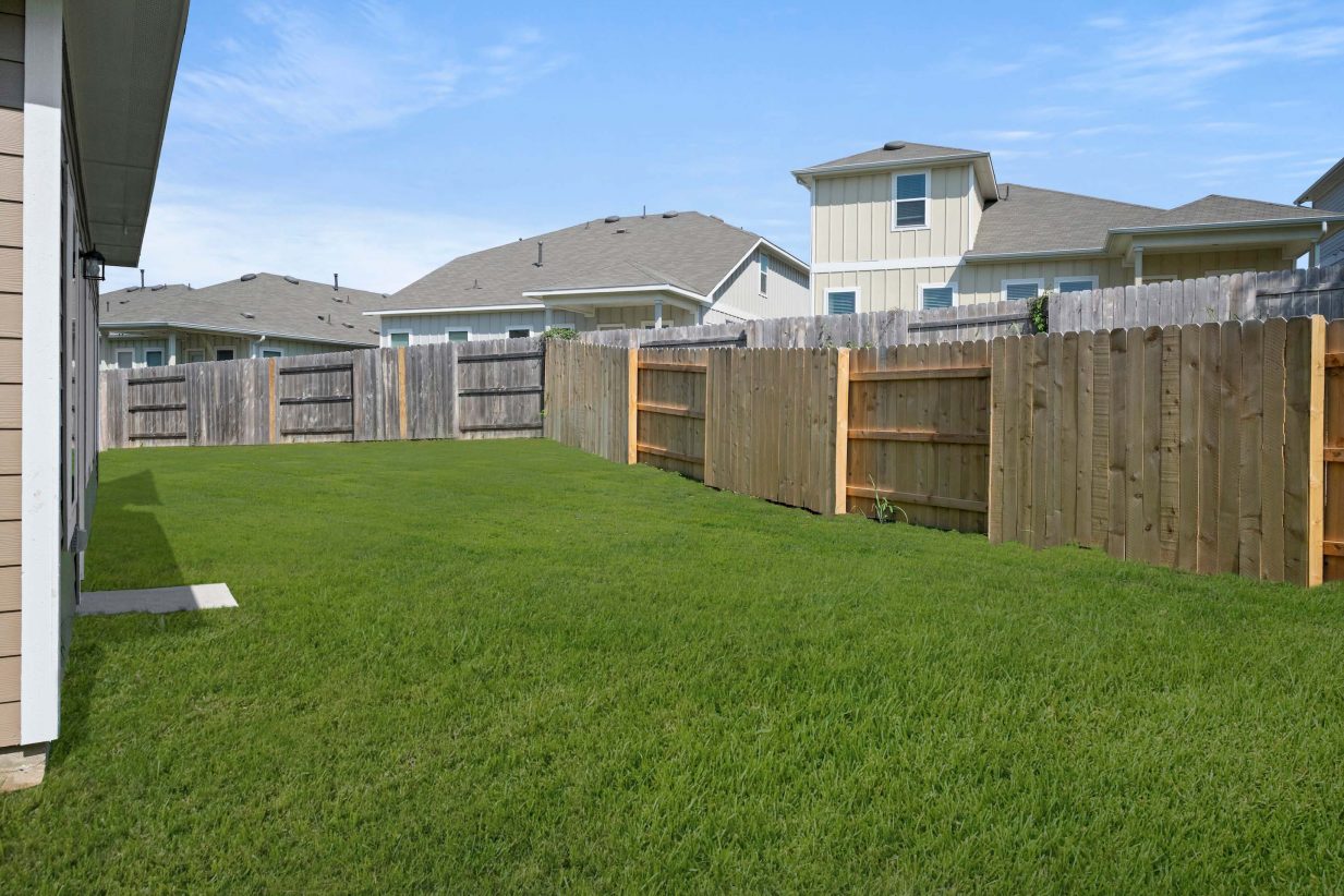 Backyard with green grass and brown fence.