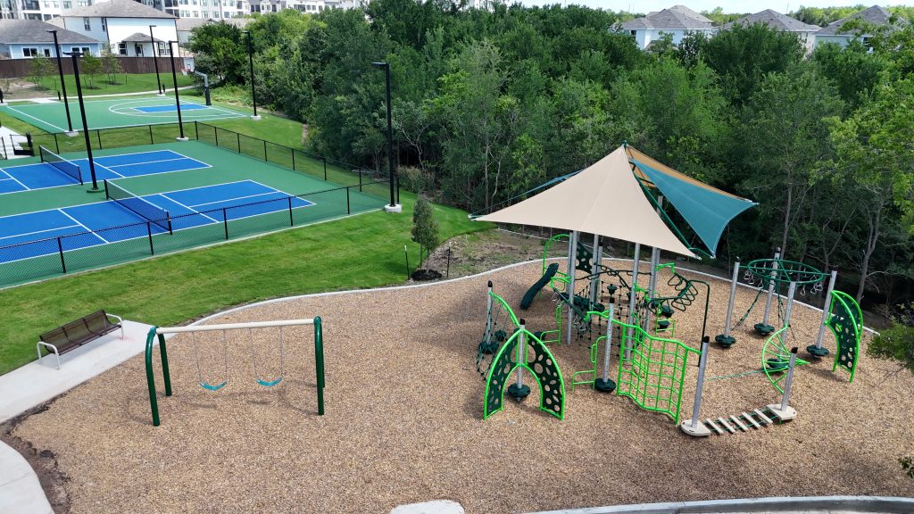 Aerial photo of community playground including swing set, and sports court with trees