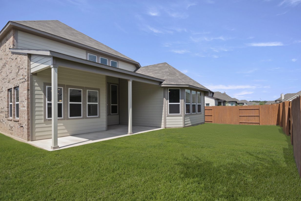 Backyard of brick two-story home with green grass and brown fence.