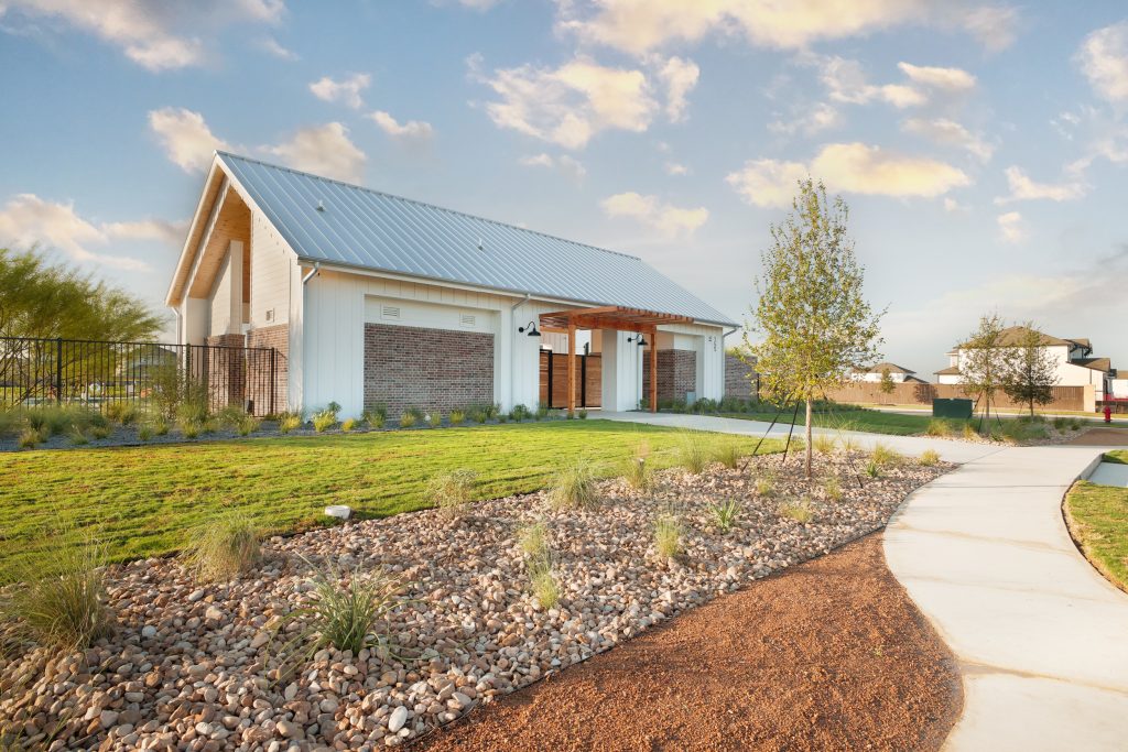 Photo of amenity center building in Brohn Homes Hymeadow in Maxwell, TX. Landscaping including natural rocks, plants, grass, granite, and a sidewalk.
