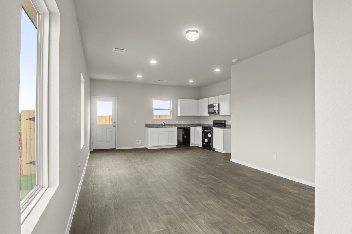Image of home interior with wood-look floor, windows, and kitchen in rear