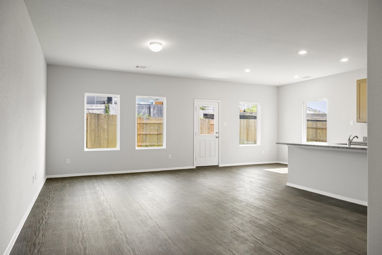 A living room with vinyl flooring, white painted walls, white-framed window, and a white door.
