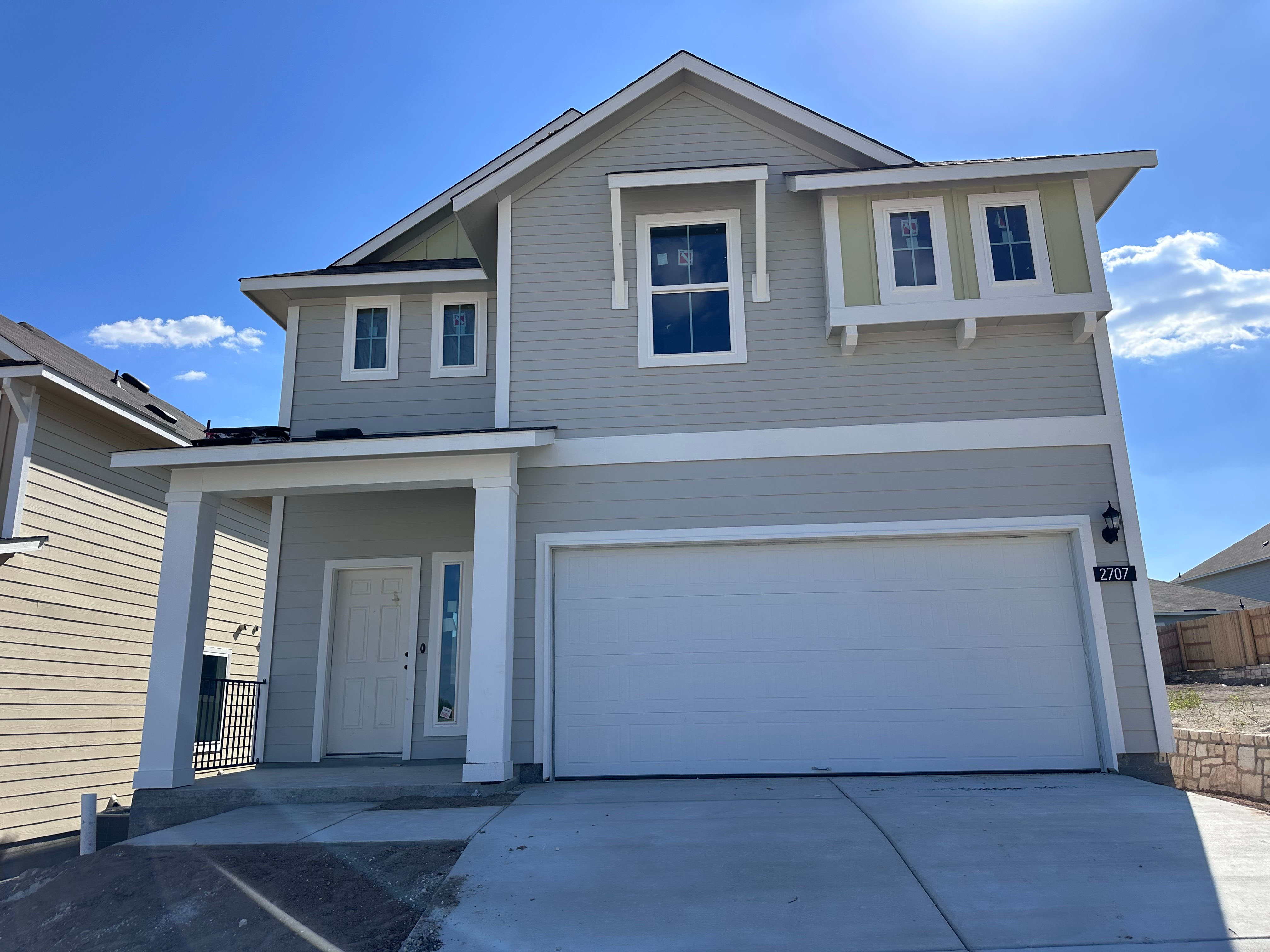 An image of grey and yellow two-story home with a white garage, driveway, dirt landscape, and blue sky in the background.