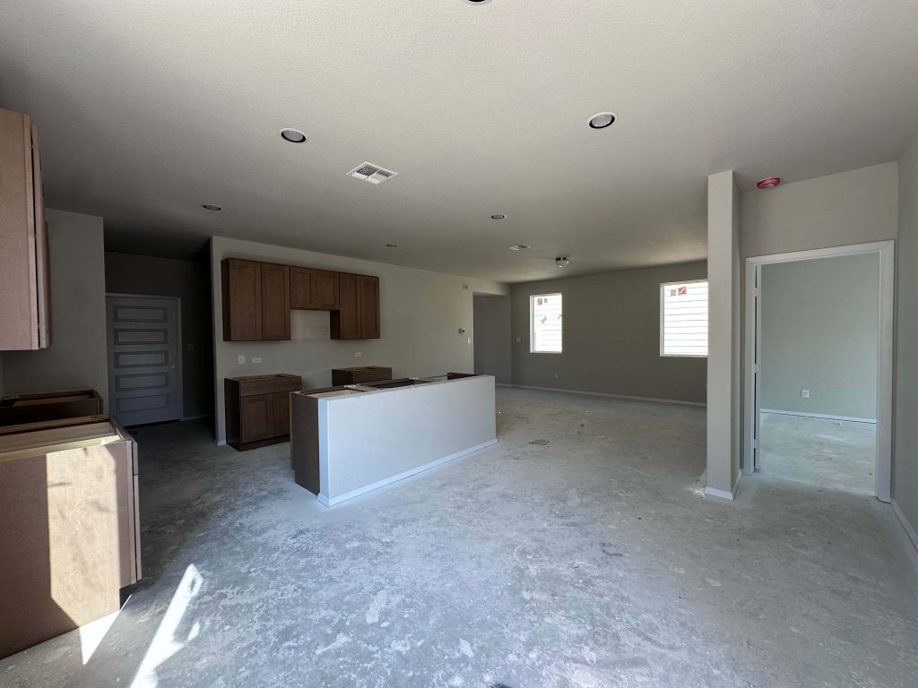 An image of kitchen and living room under construction with brown cabinets and cream painted walls.