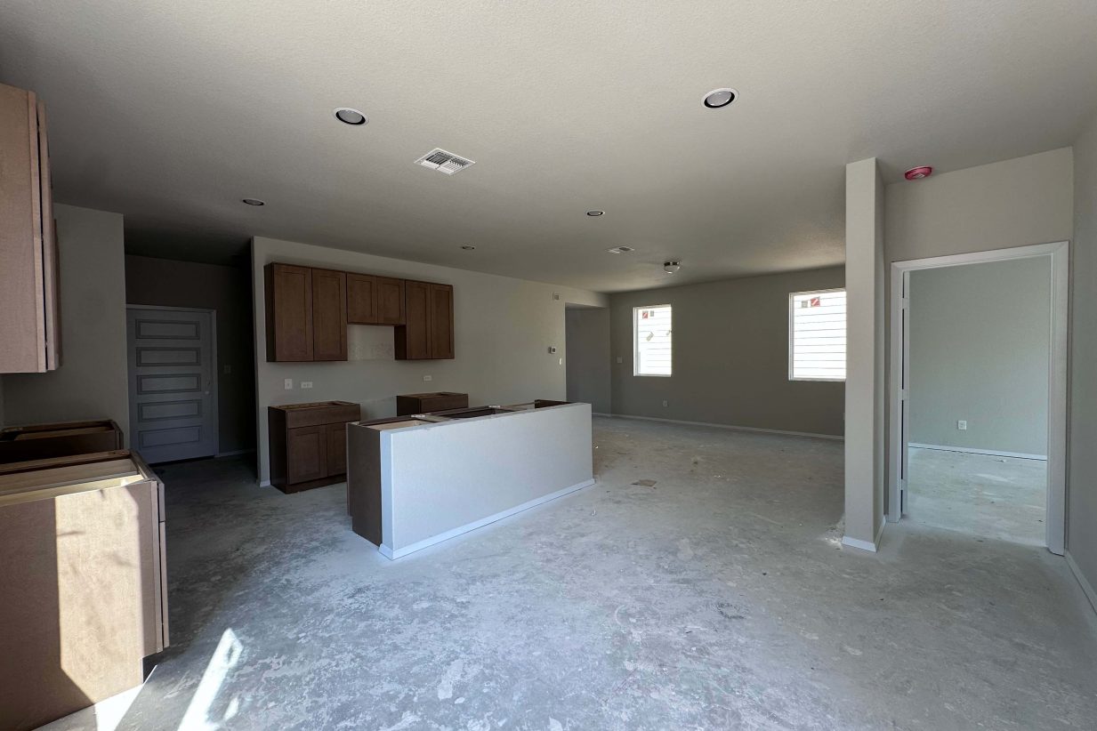 An image of kitchen and living room under construction with brown cabinets and cream painted walls.
