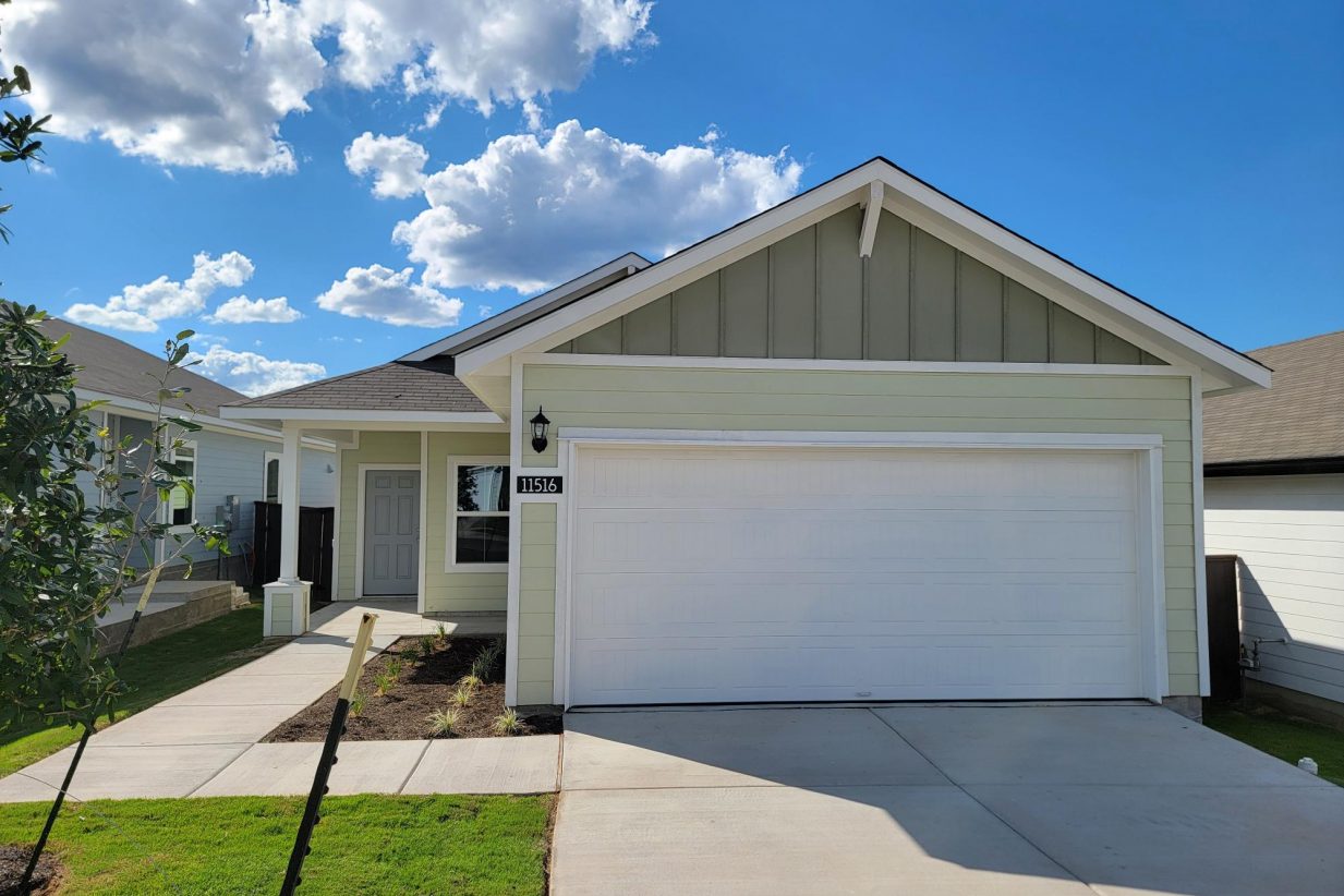Image of one story yellow home with white accents and garage, green grass, and sky