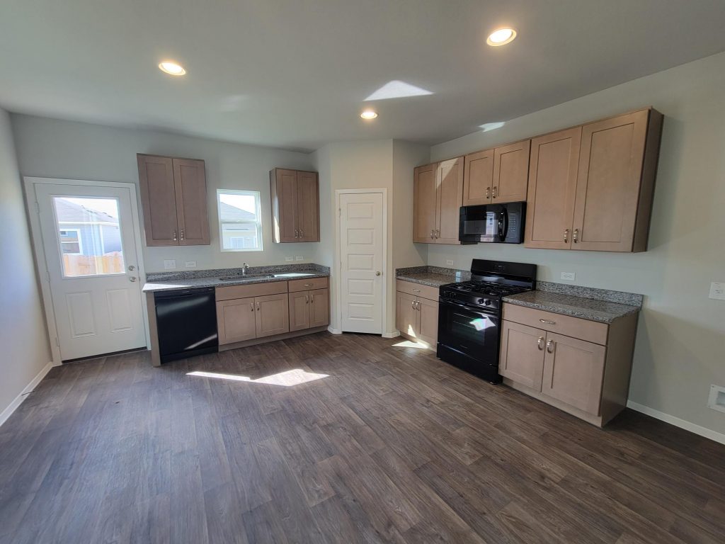 Image of home kitchen with wood-look floor, light brown cabinets, window over sink and in rear door, white walls, and black appliances