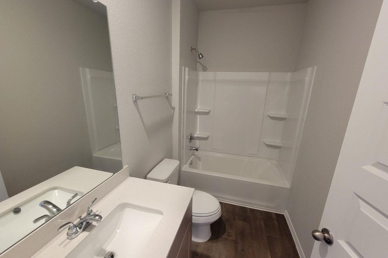 Image of home secondary bathroom with mirror, vanity with white countertop and light brown cabinet, wood-look floor, toilet, and tub