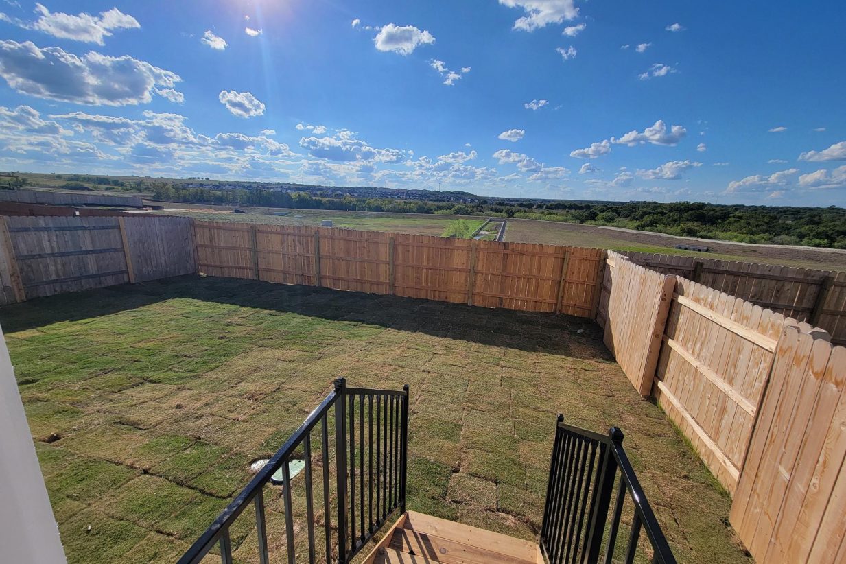 Image of home back yard with wood steps, railing, grass, wood fencing, and sky