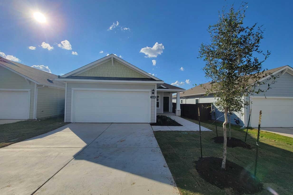 Image of one story yellow home with white garage, tree, grass, and sky
