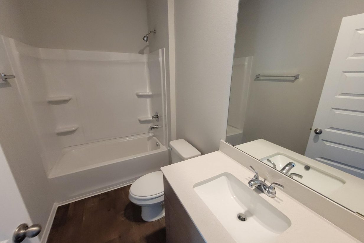 Image of home bathroom with vanity, mirror, toilet, and bathtub with wood-look flooring and white walls