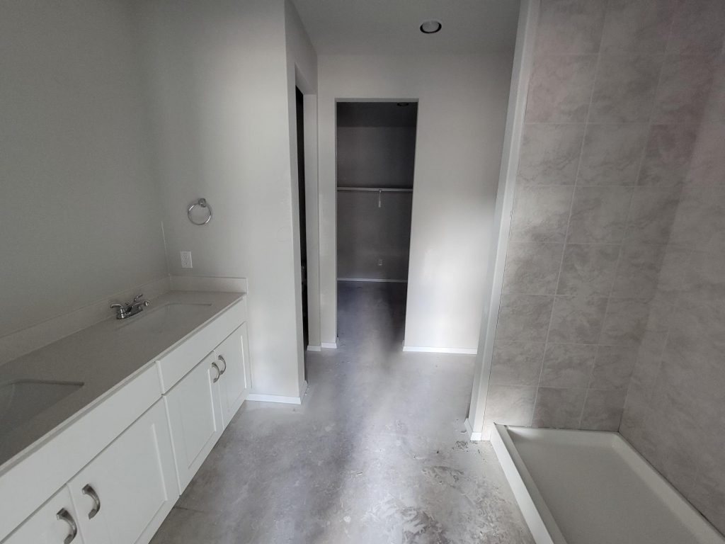 Image of home bathroom under construction with vanity with white countertop and cabinets, shower, and doorway to walk-in closet