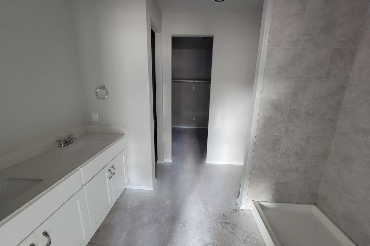 Image of home bathroom under construction with vanity with white countertop and cabinets, shower, and doorway to walk-in closet