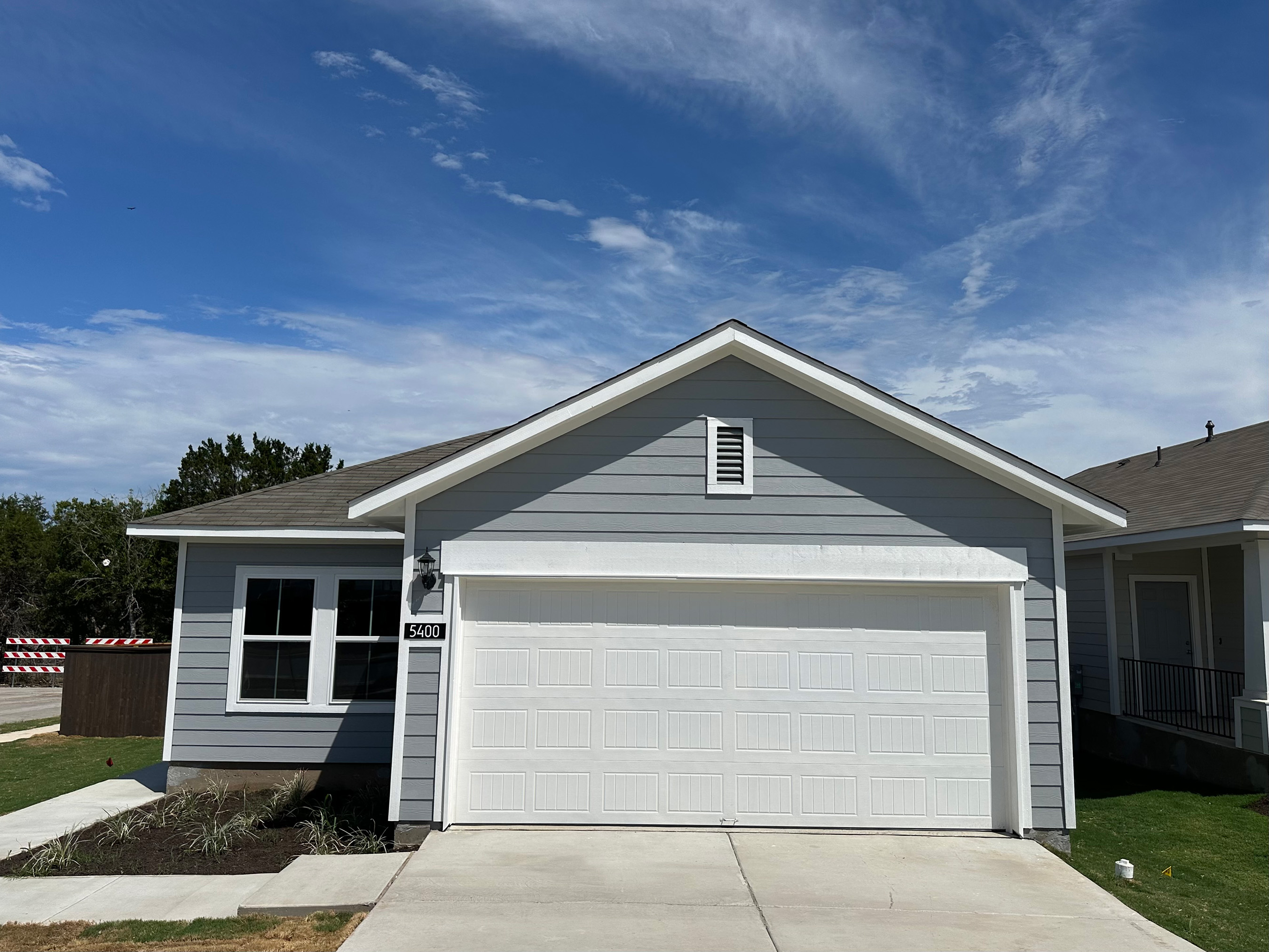 Exterior of one story slate grey home with white traim and garage door with driveway and sky