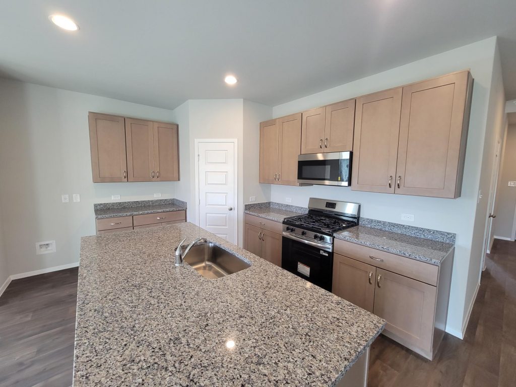 Image of home kitchen with light brown cabinets, stainless steel appliances, and center island with white walls