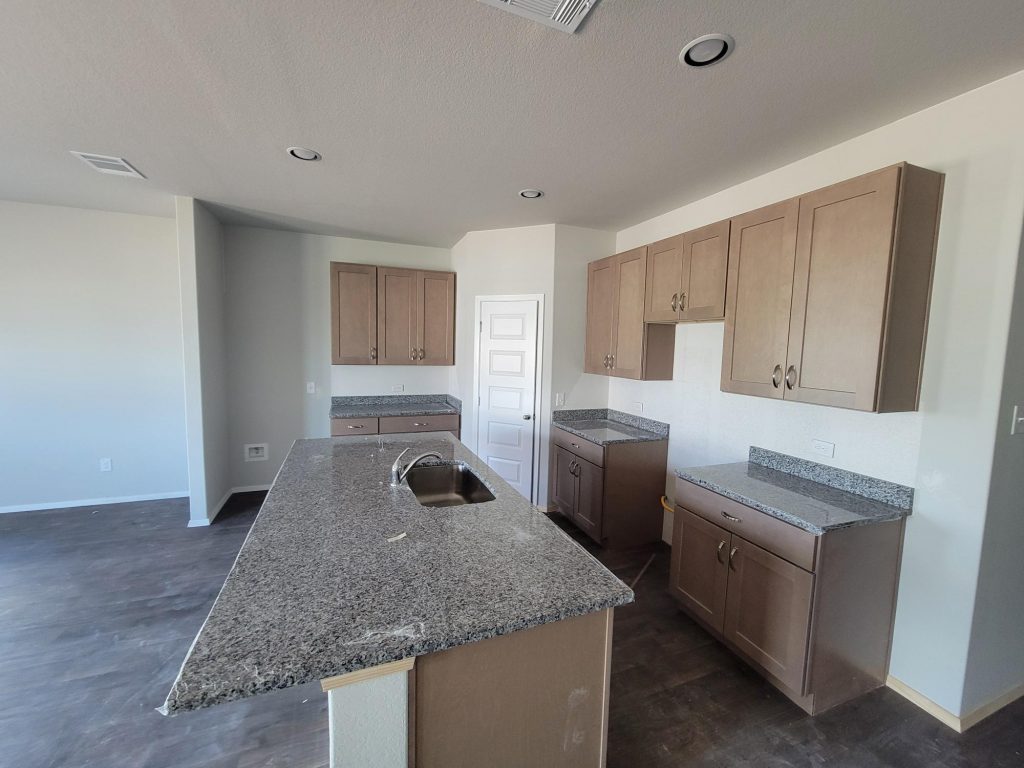 Image of home kitchen with center island, light brown cabinets, white walls, and wood look floor