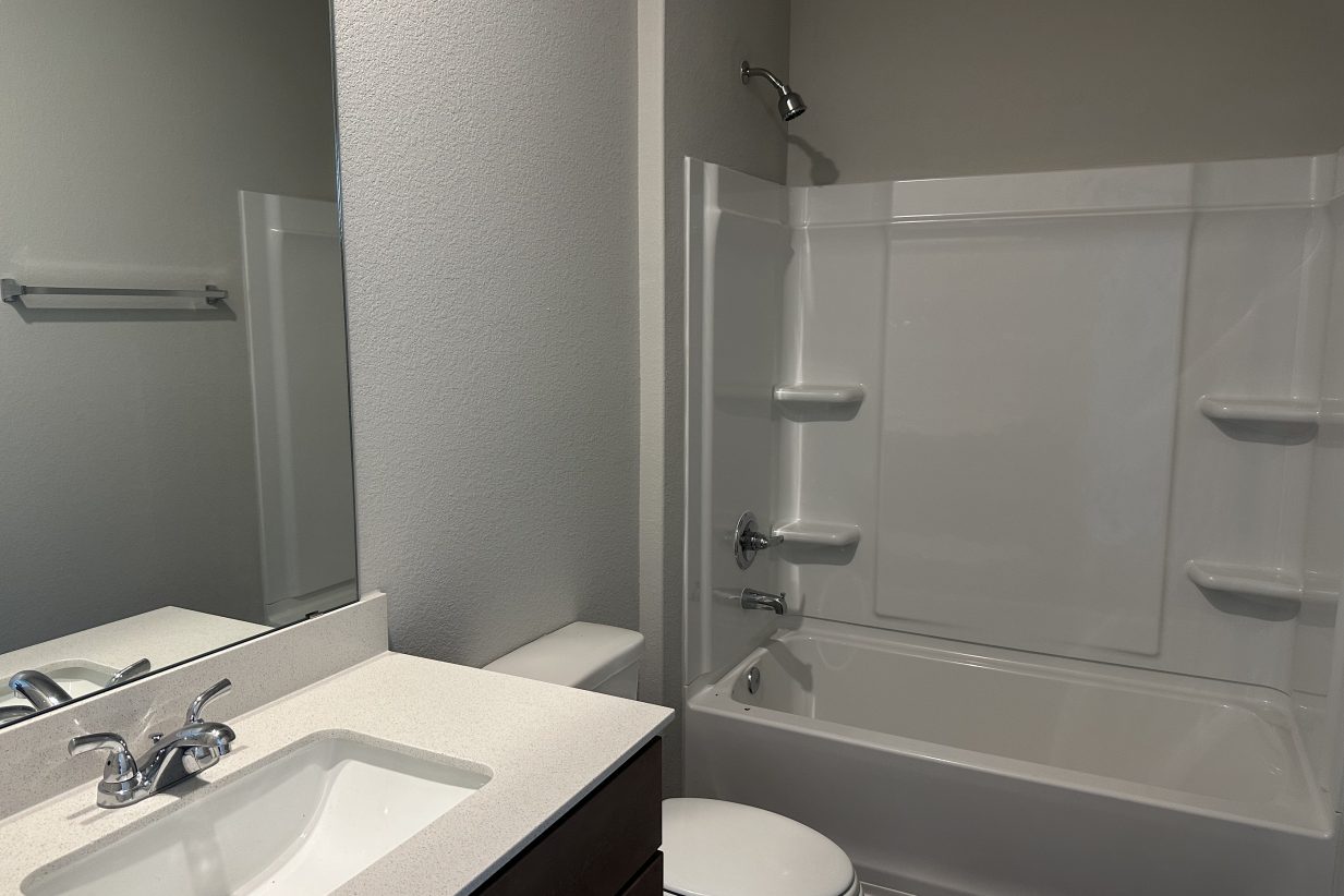 Image of bathroom with vanity with white countertop and light brown cabinet, toilet, and bathtub