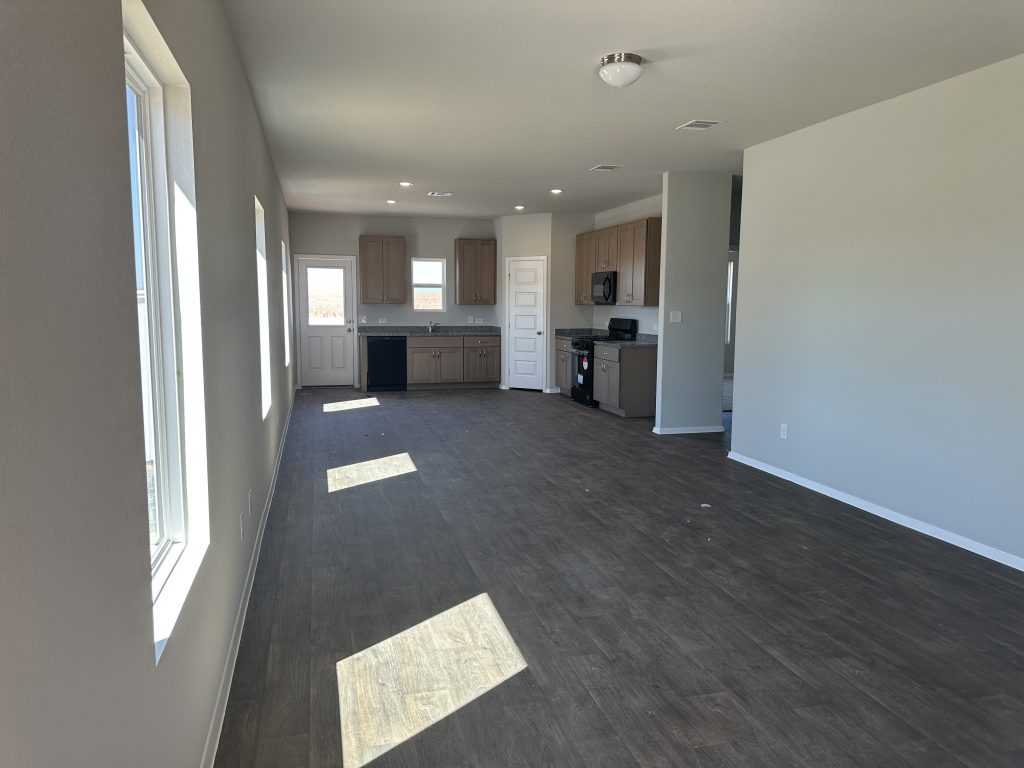 Image of living spaces with windows, wood-look vinyl flooring, and kitchen in rear