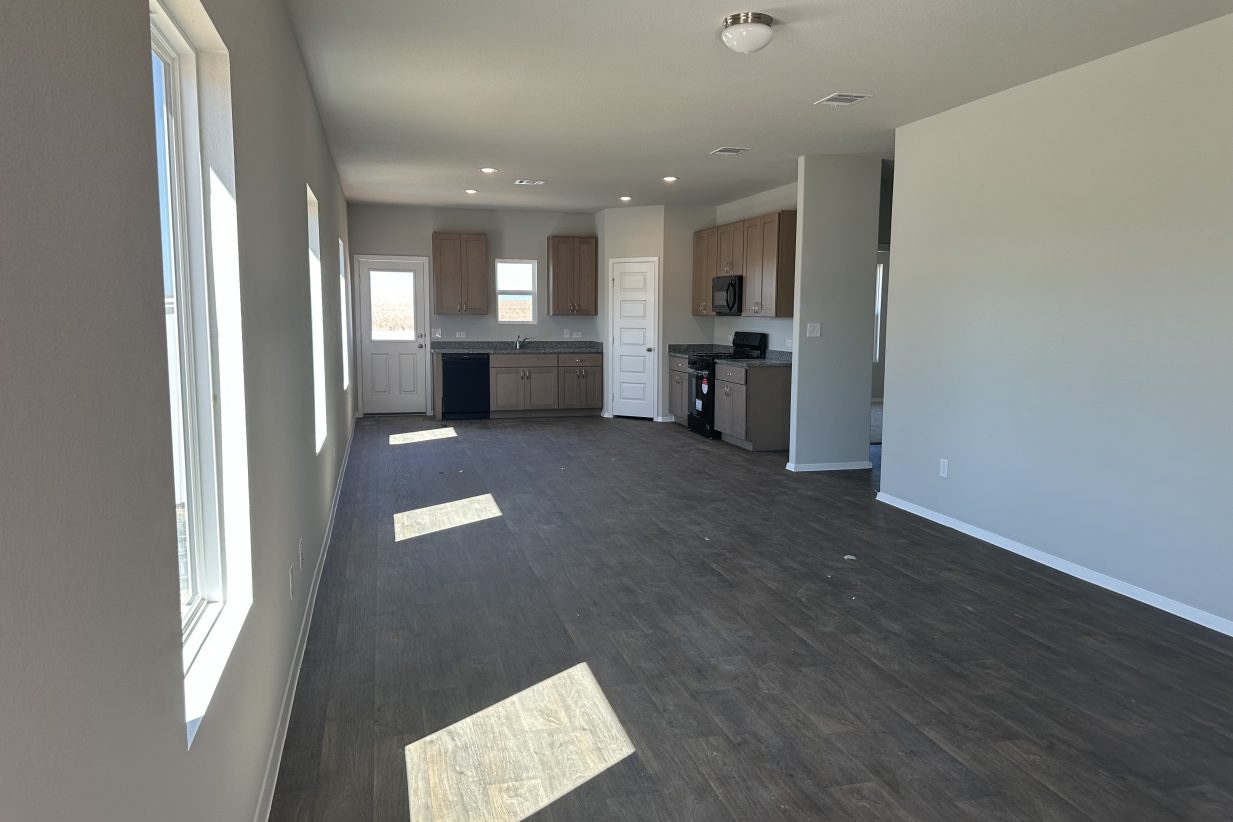 Image of living spaces with windows, wood-look vinyl flooring, and kitchen in rear