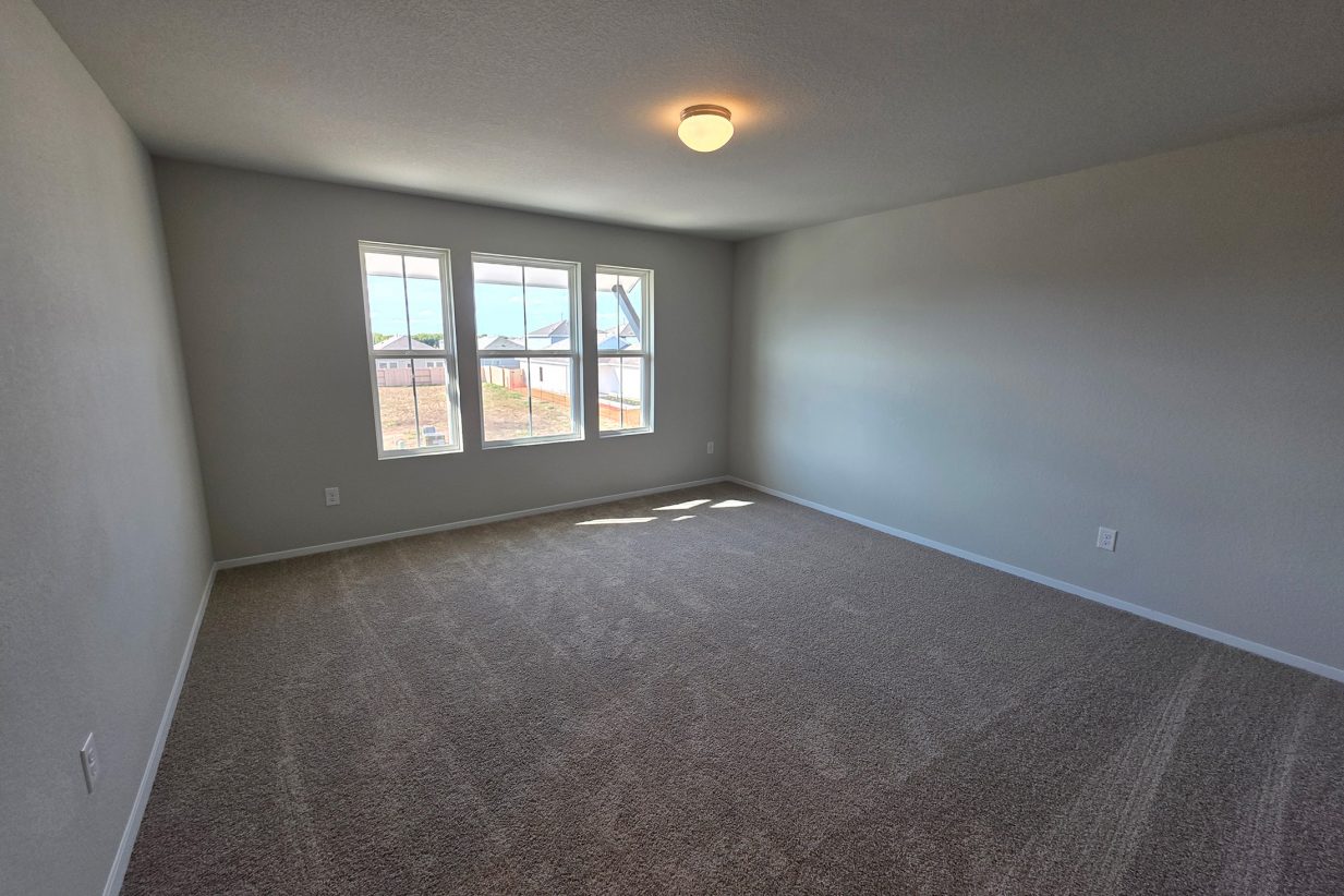 Image of home primary bedroom with windows on one wall, light walls, and tan carpet