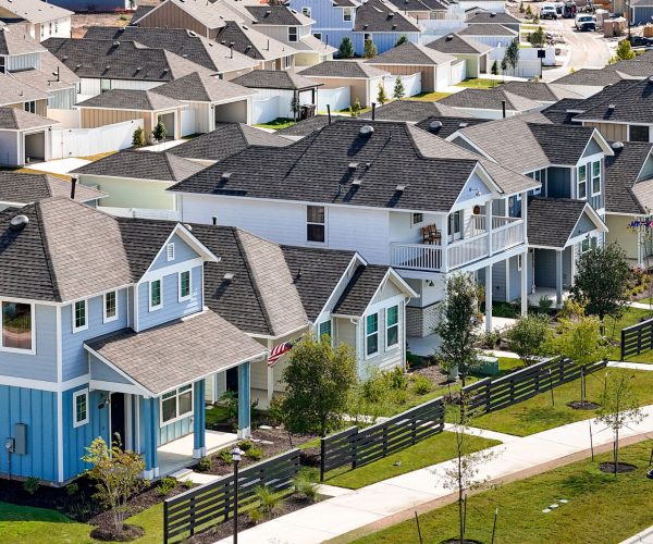 A Street view of two-story and one-story next to fence and sidewalk.