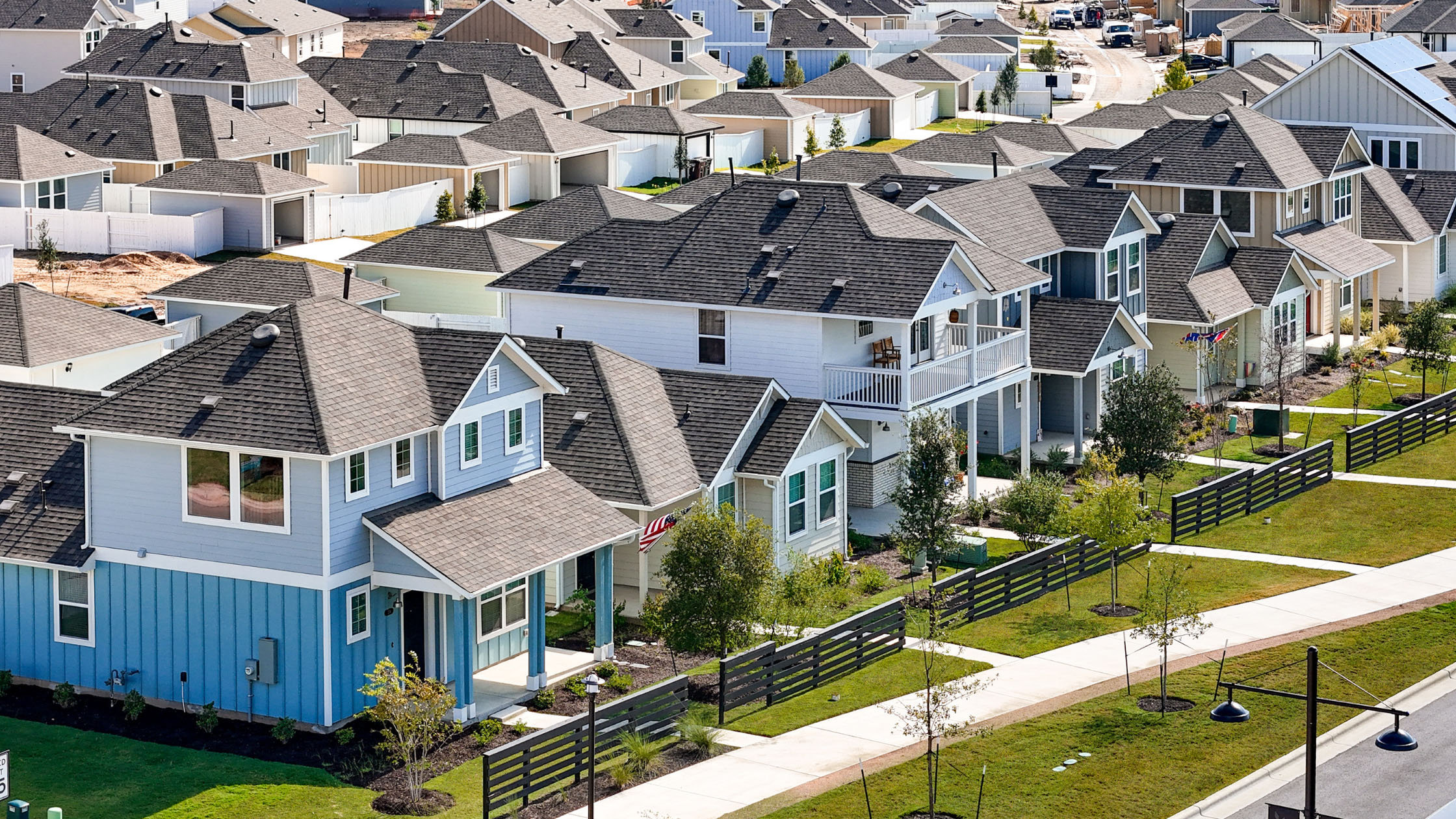 A Street view of two-story and one-story next to fence and sidewalk.