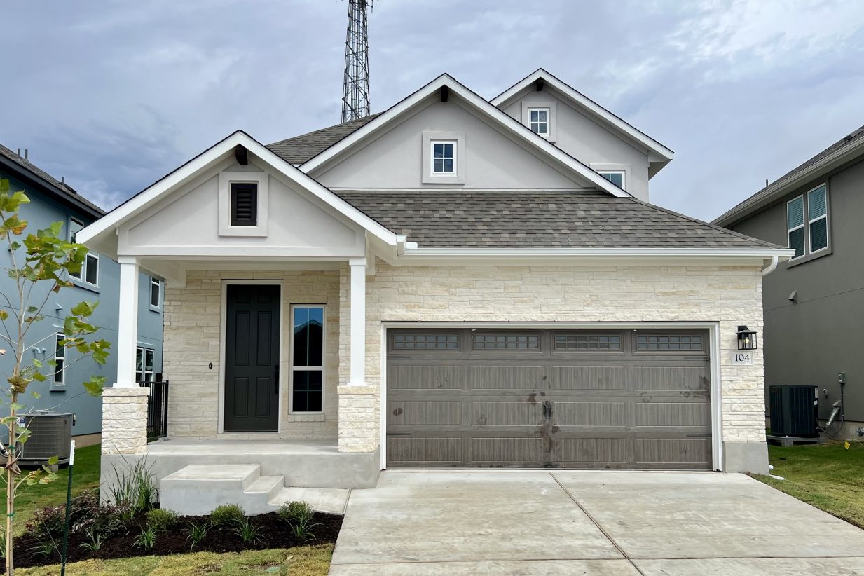 Front exterior of two-story house with a brown garage door with a driveway and green landscape.
