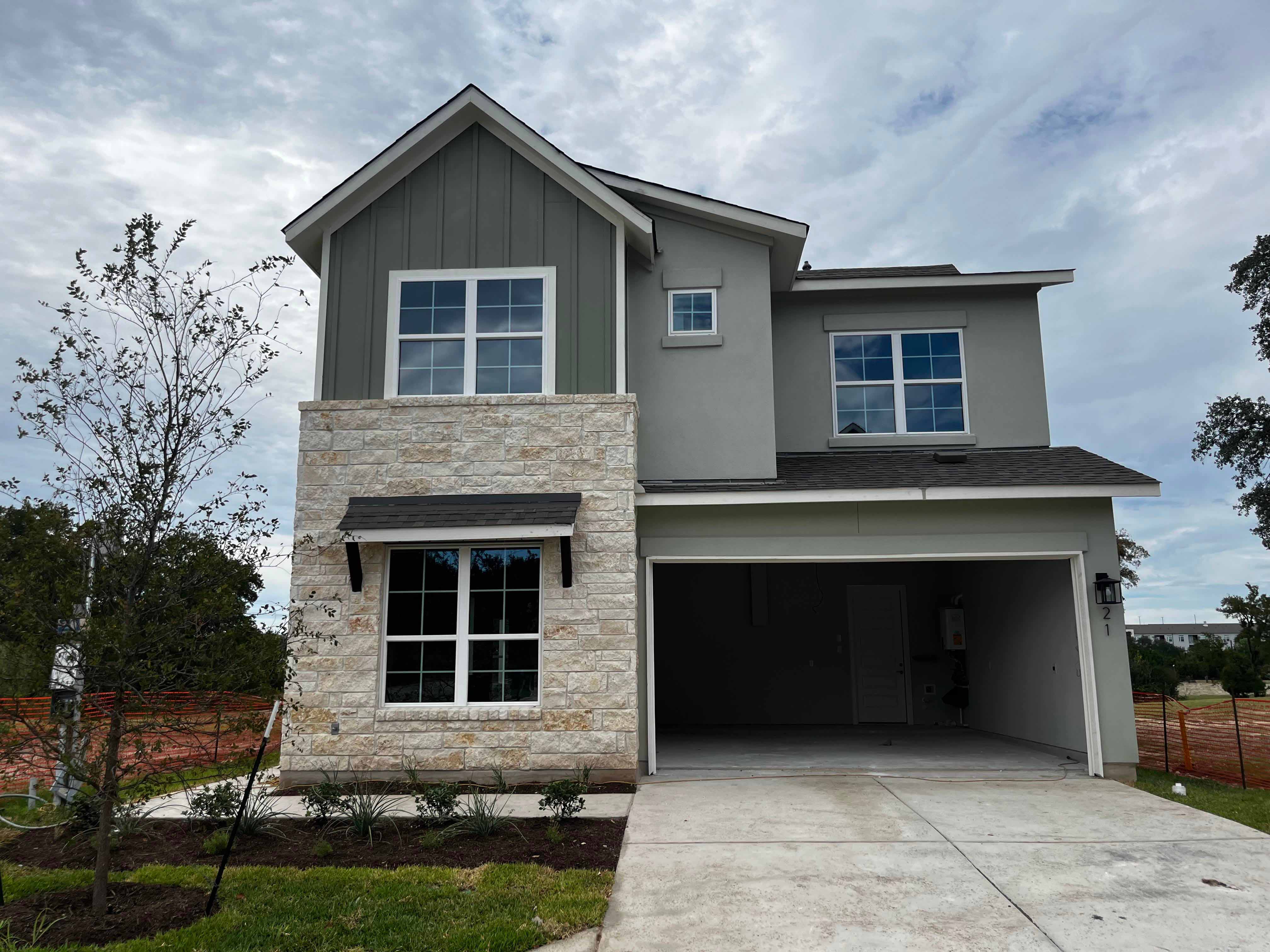 Image of front of a green two-story house with brick accents, open garage door, and green landscape.