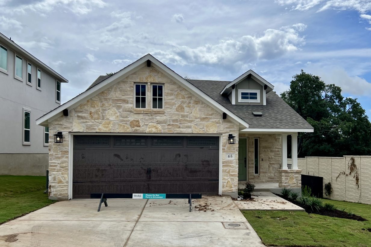 Front exterior image of brick house with brown garage door, driveway, and green landscape.