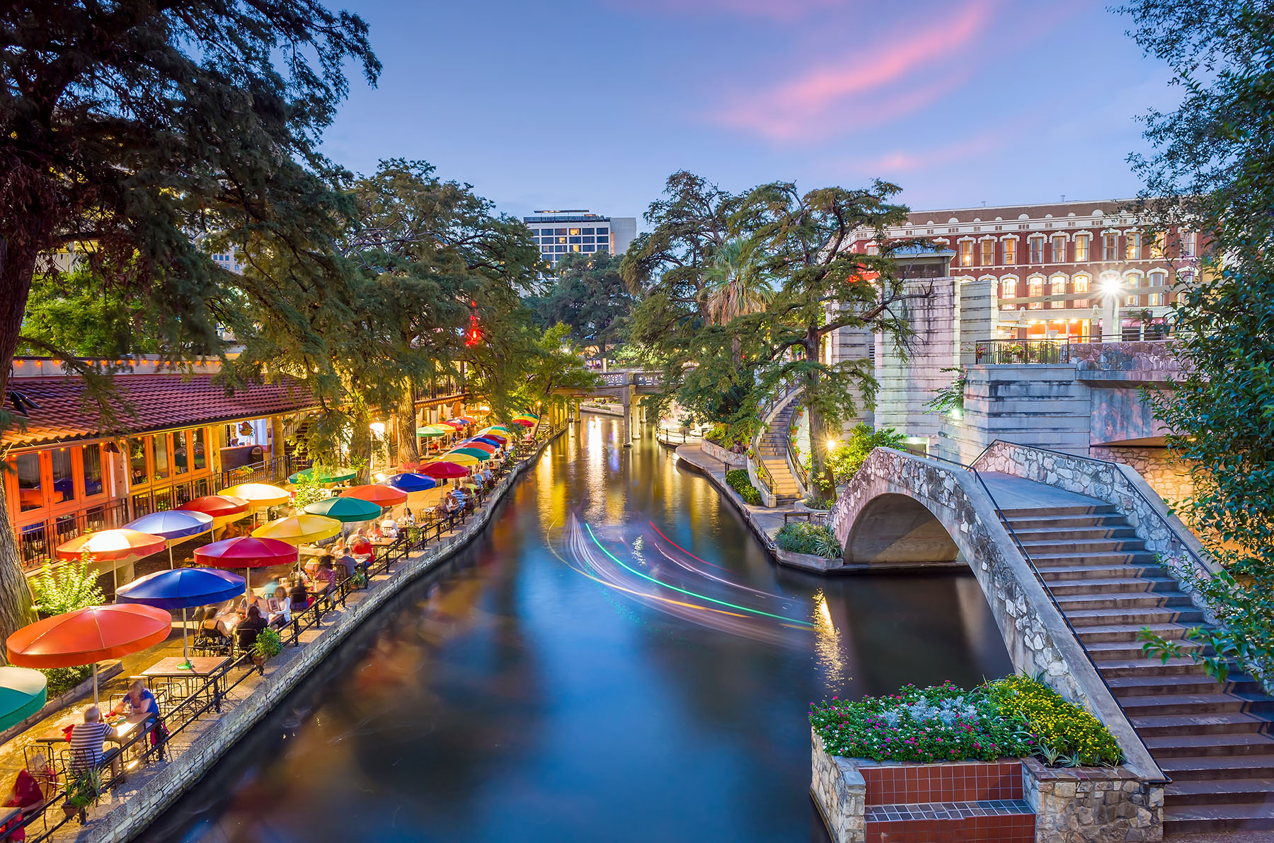 The San Antonio Riverwalk with vibrant colored umbrellas and a bridge over a river.